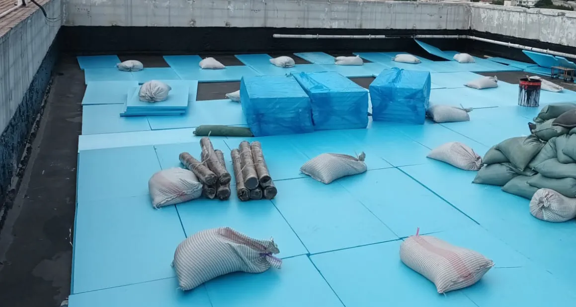 薄扶林道碧瑤灣工程：以沙包、施工管線及磚塊壓穩藍色板材的天台近景