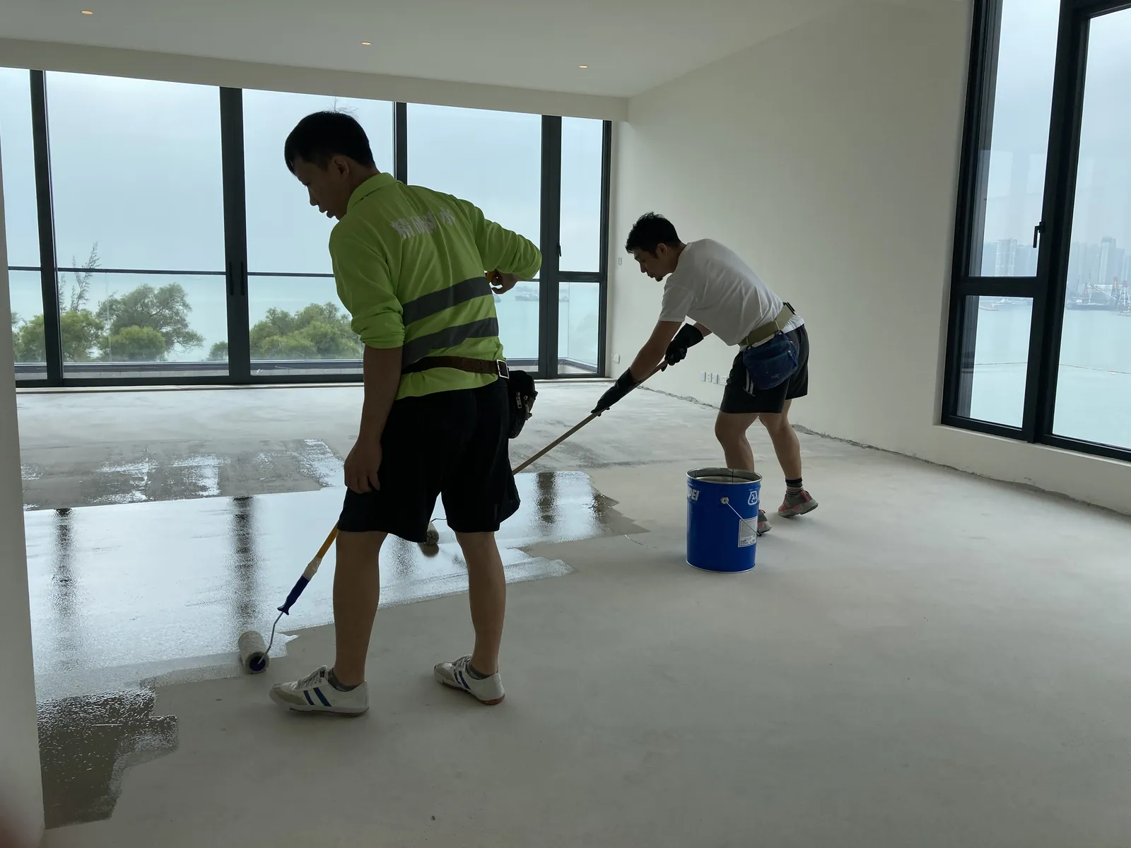 屯門瑧譽臨海住宅內,兩名工人在落地玻璃窗旁以滾筒處理地面