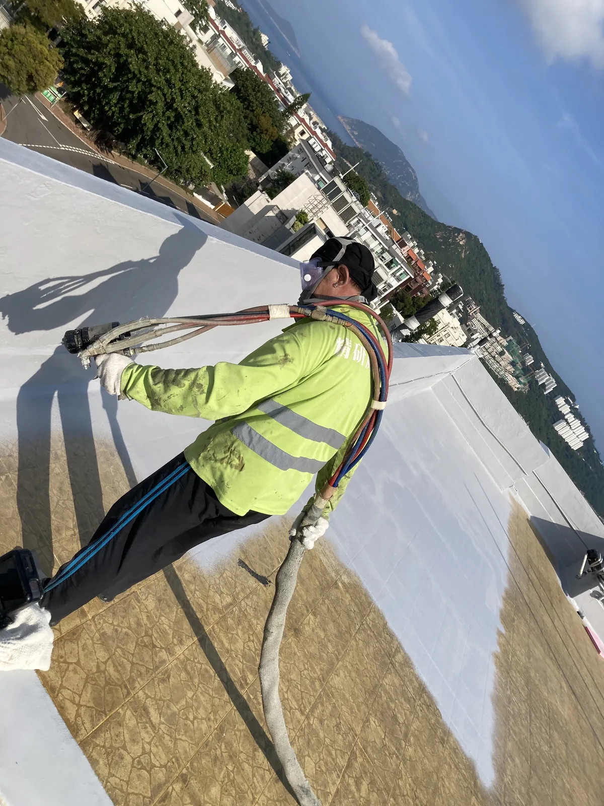 Worker rolling a light-coloured material along a rooftop edge at Bauhinia Gardens, Chung Hom Kok