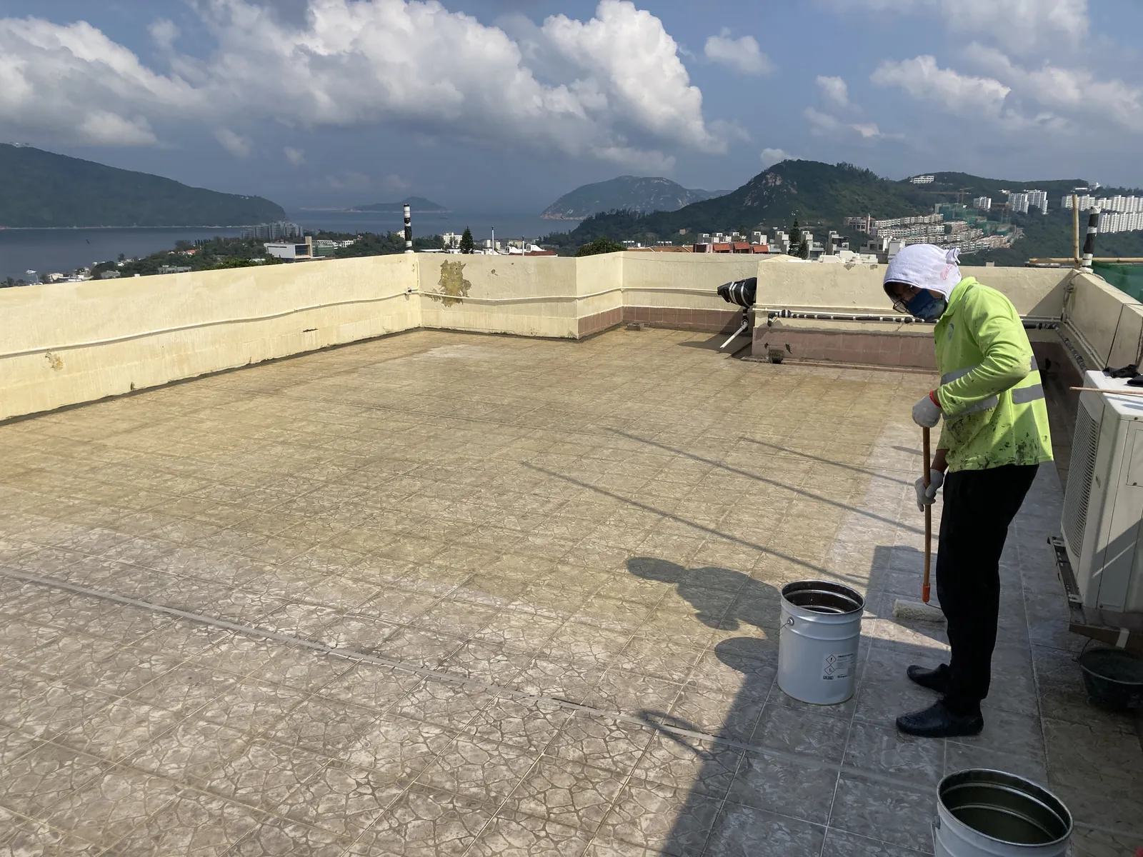 Worker carrying out surface work on the patterned rooftop beside equipment at Bauhinia Gardens