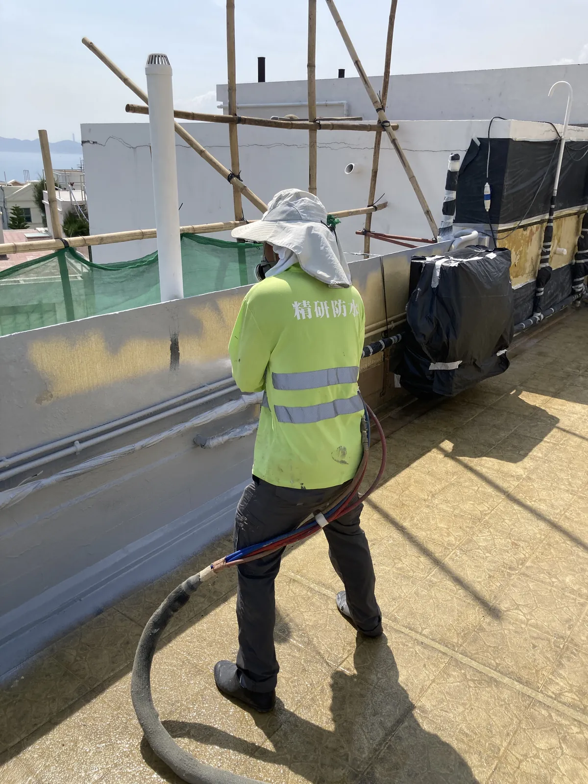 Worker using spray equipment to treat the rooftop wall base and equipment surrounds at Bauhinia Gardens