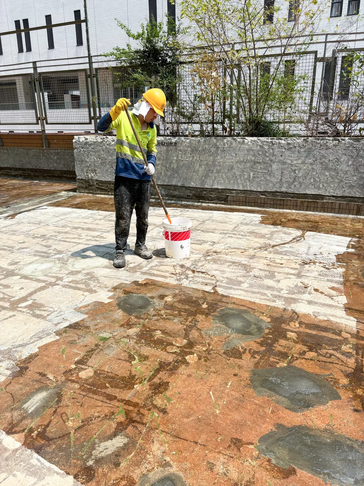 A worker mixes site material beside several grey treated areas on a roof at Hong Kong Baptist University in Kowloon Tong.
