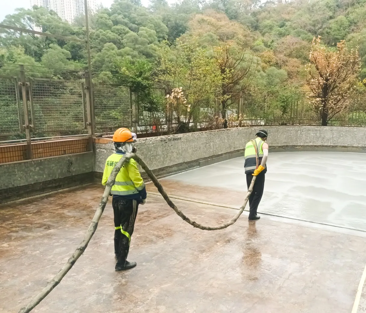 Two workers use a hose and long-handled tool across a large roof area at Hong Kong Baptist University in Kowloon Tong.