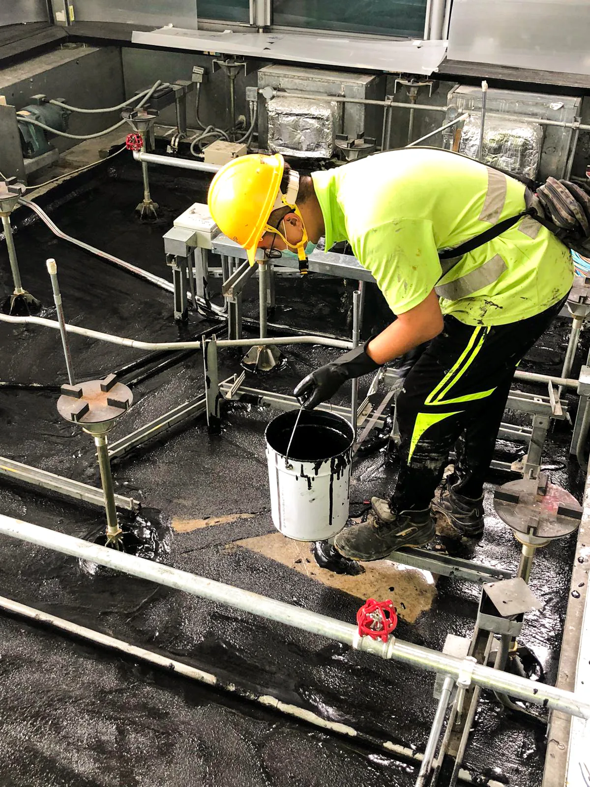 中環匯豐銀行總行內，工人在管道及設備之間以手工具處理深色地面
