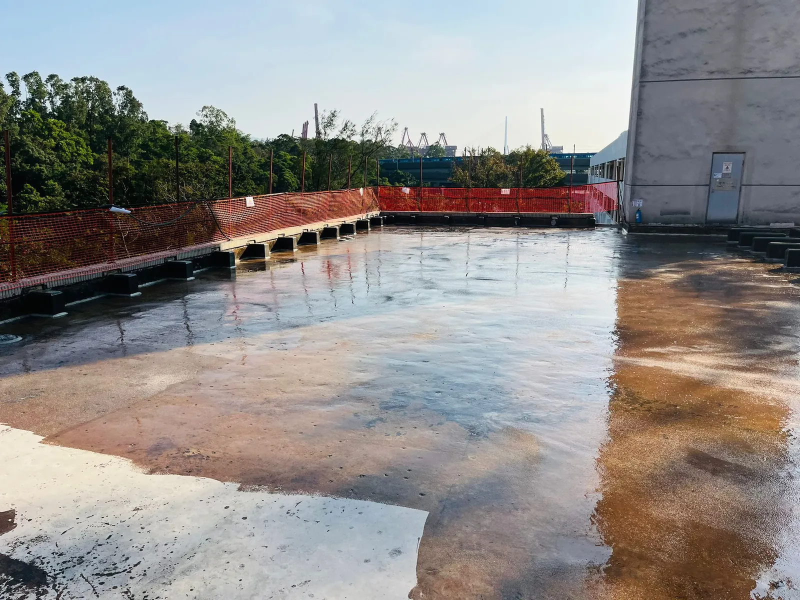 葵涌火葬場屋面大面積濕潤反光表面、灰色凸起基座及橙色安全網