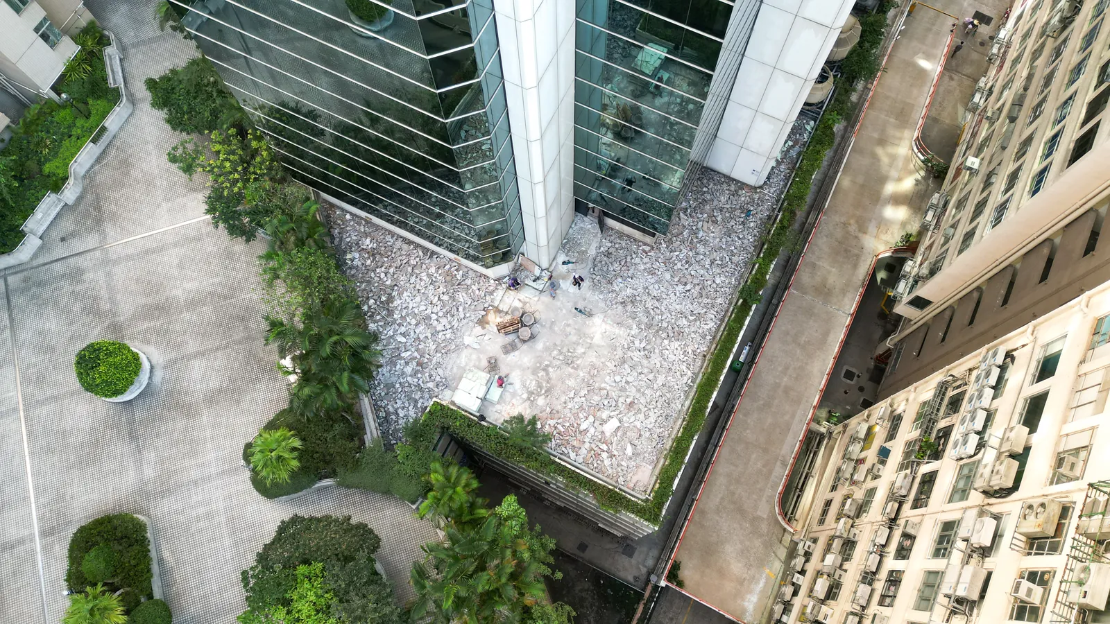 高處俯瞰炮台山理文商業中心玻璃大樓旁的平台，可見淺色碎塊及數名工人