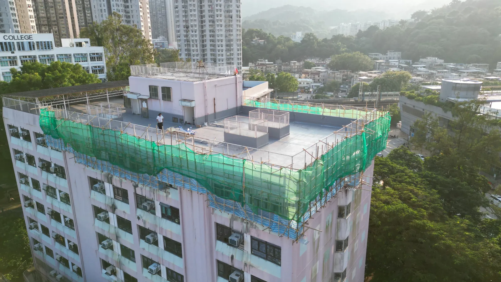 樂善堂粉紅色大樓航拍，天台周邊為綠網棚架並有工人在屋面作業