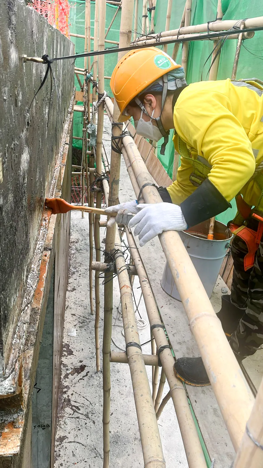 Worker on bamboo scaffolding applying a dark coating to an external wall at No. 3 Middle Gap Road