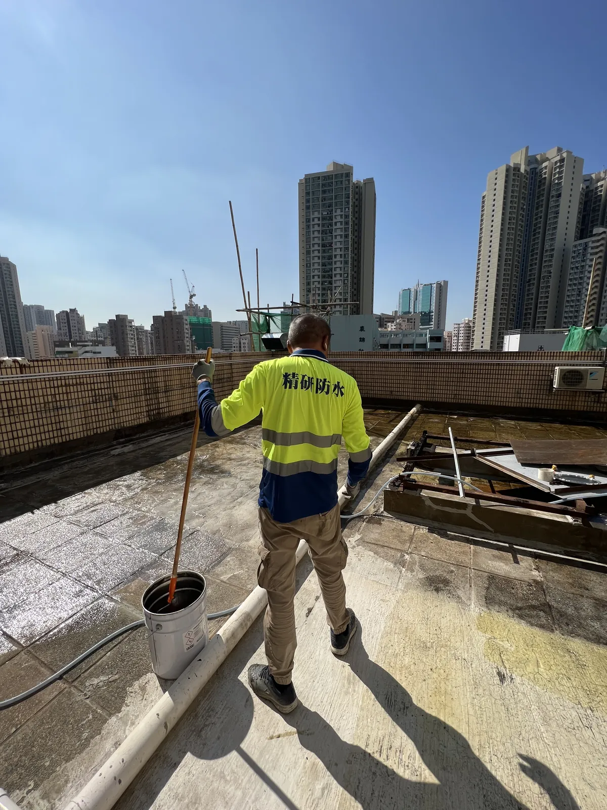葵涌安蔭商場施工人員手持長桿和水桶走過天台，地面呈現深淺不同區域