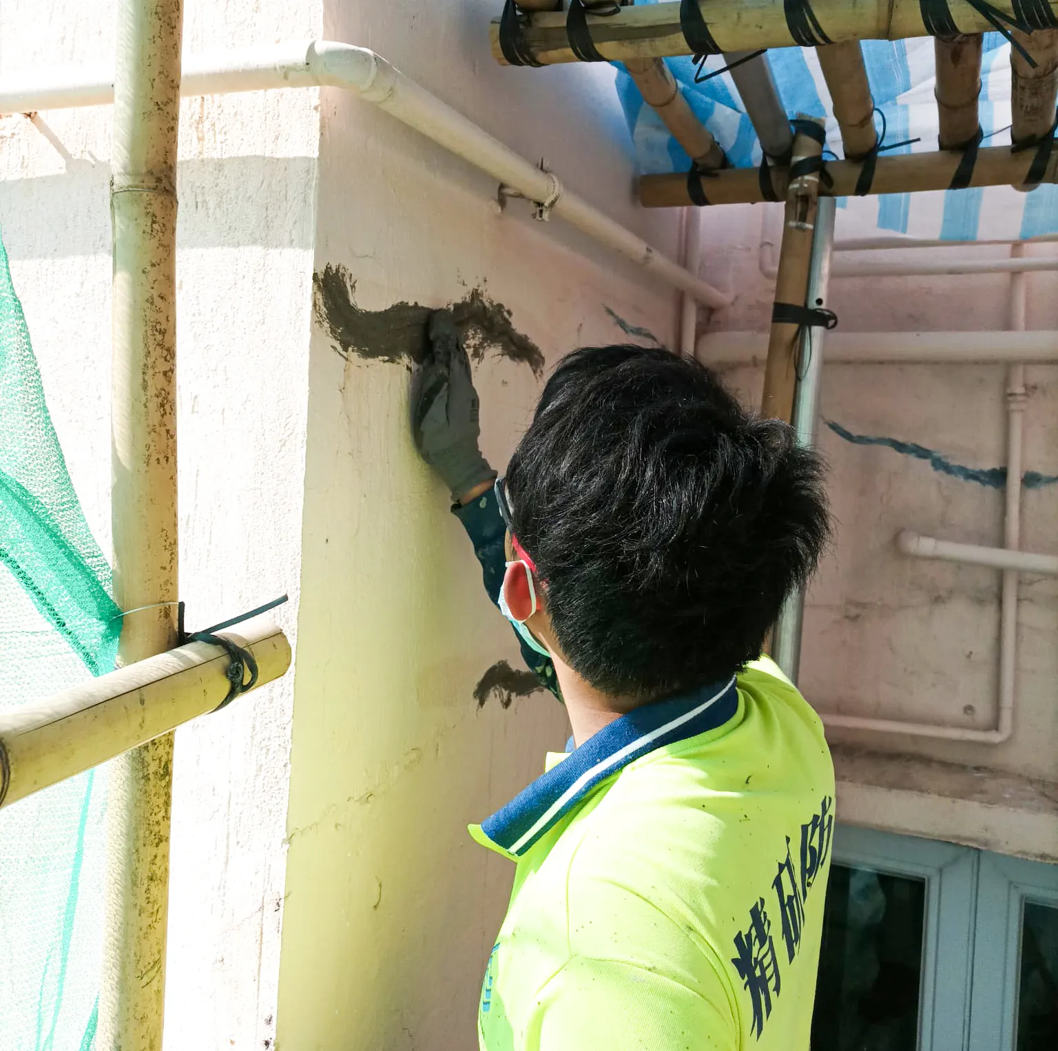 太子運動場道工人在棚架內以手工具處理管道旁的外牆位置