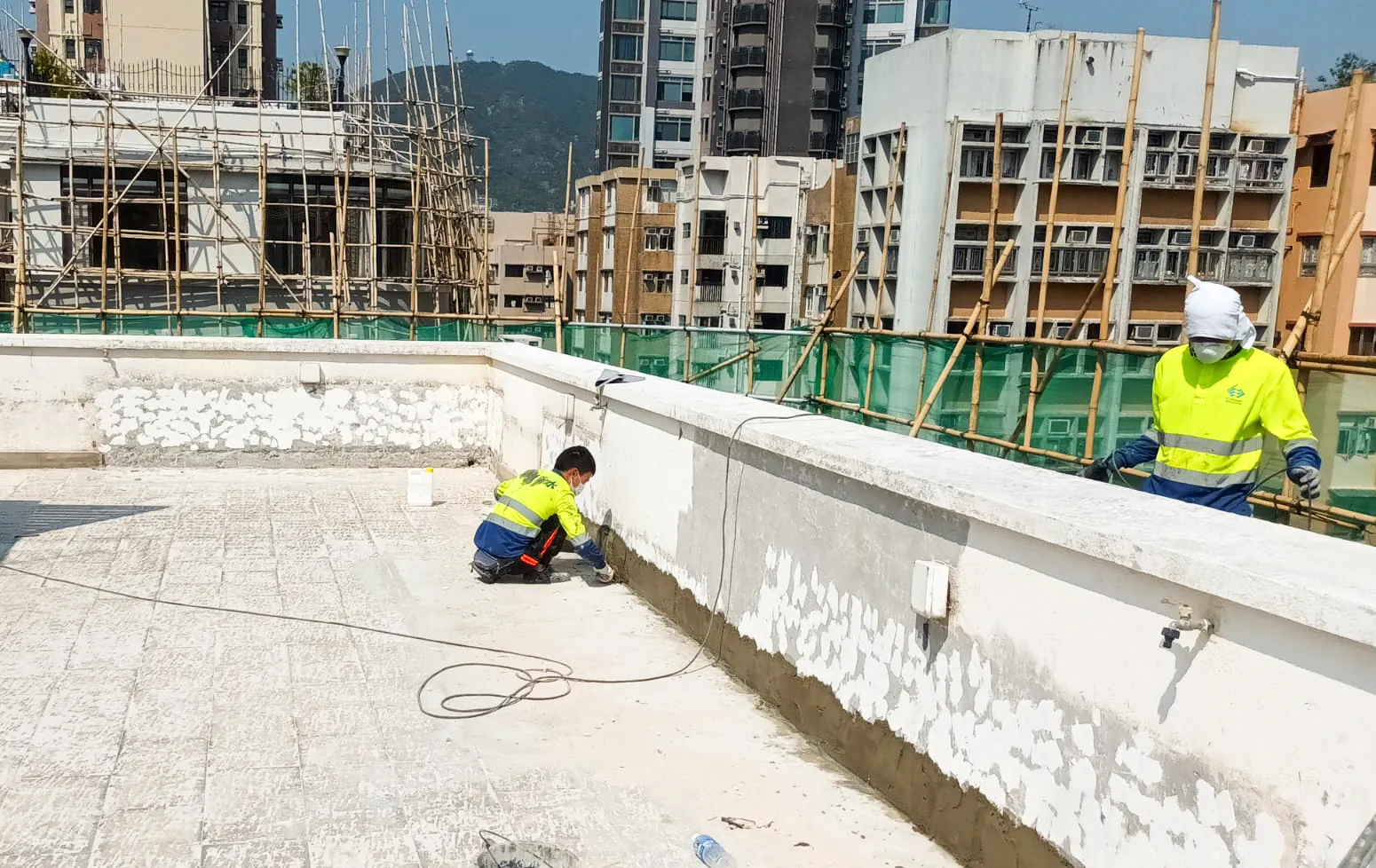 太子運動場道兩名工人處理天台女兒牆牆腳，牆面可見剝落和斑駁痕跡