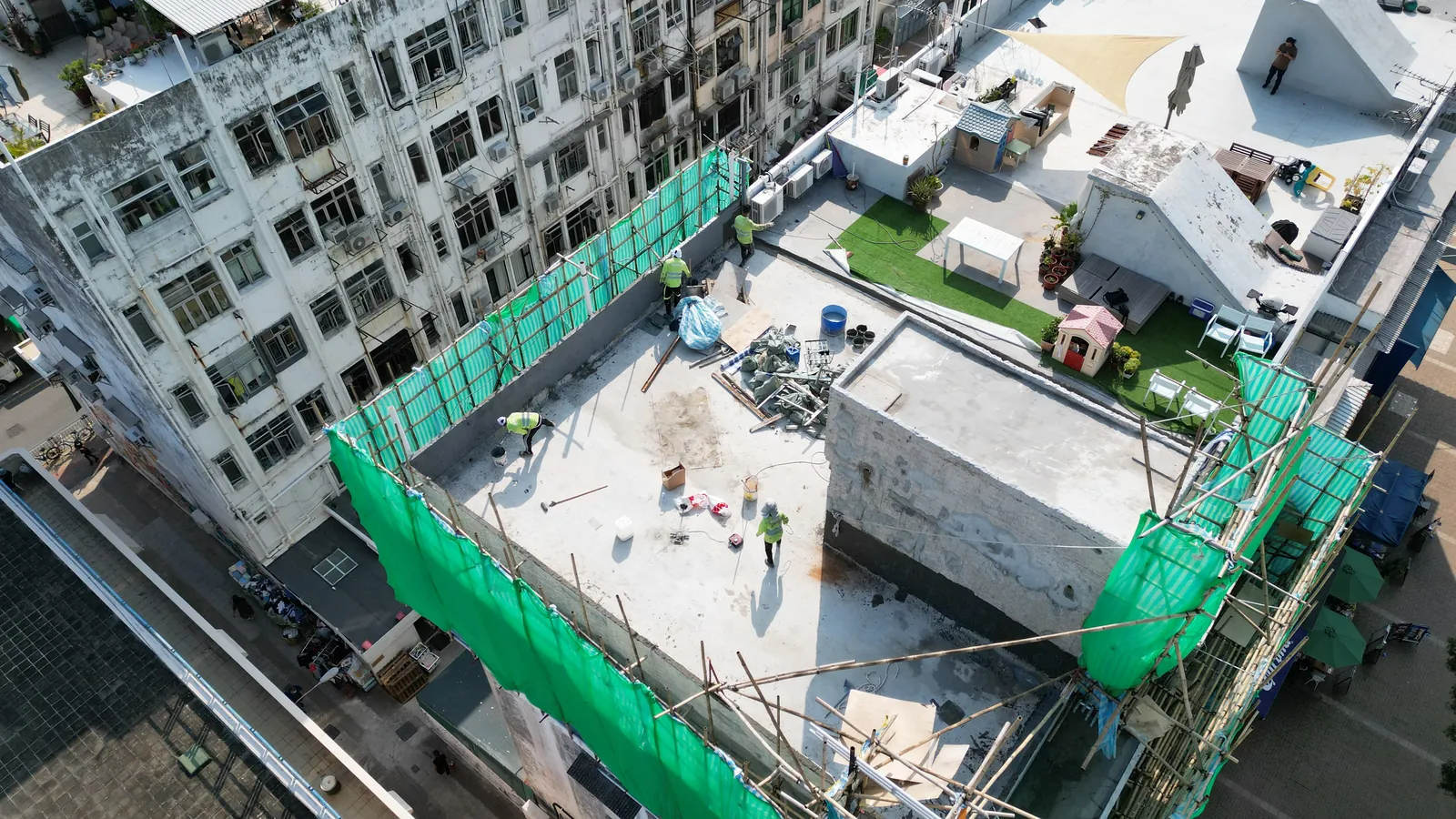 西貢灣景街天台航拍,屋面四周搭有綠網棚架並有多名工人和設備