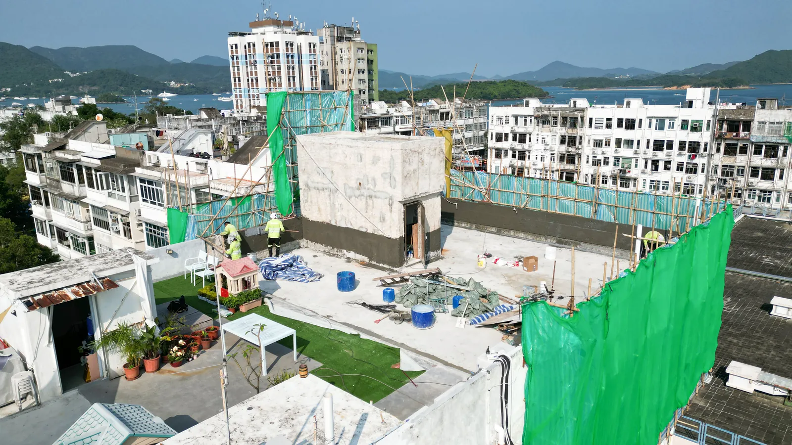 西貢灣景街天台工程全景,可見綠網棚架、工人、桶具及遠處山海景