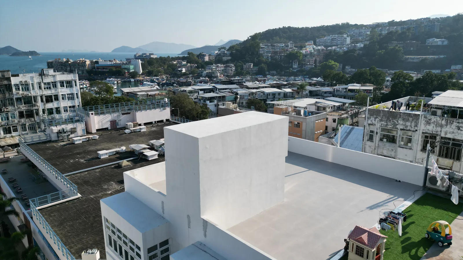 西貢灣景街白色天台斜角航拍,背景可見西貢樓宇、山坡及海岸