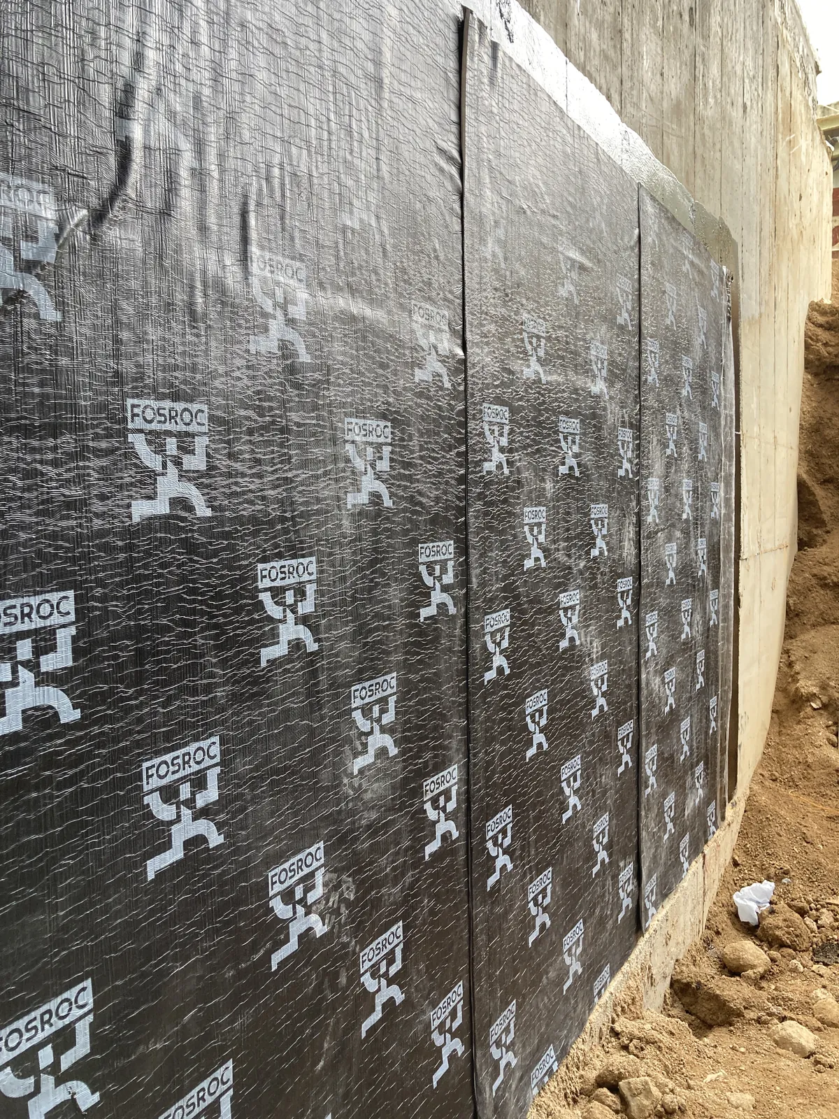 Long wall at the Villa Panova site in Sai Kung with continuous black panels and soil along the base.