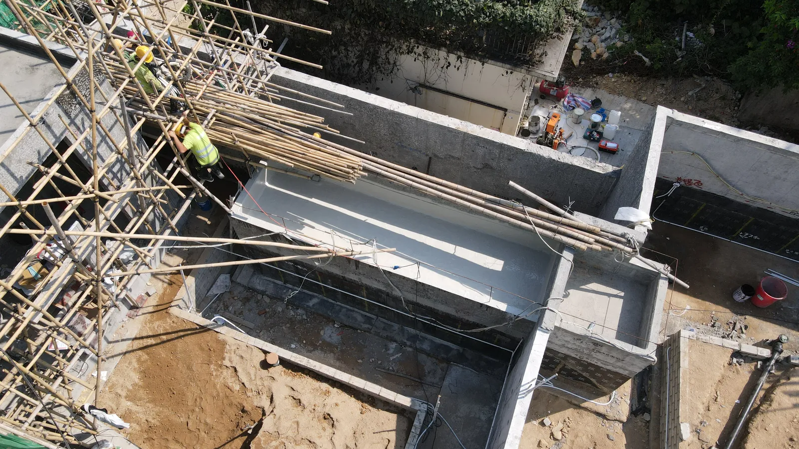 Overhead view of workers on bamboo scaffolding along a long grey wall at Villa Panova in Sai Kung.