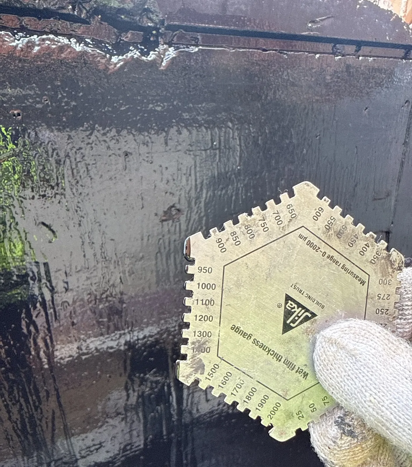 寶石湖路工程人員戴手套,將濕膜厚度梳規貼在深色防水表面作檢查