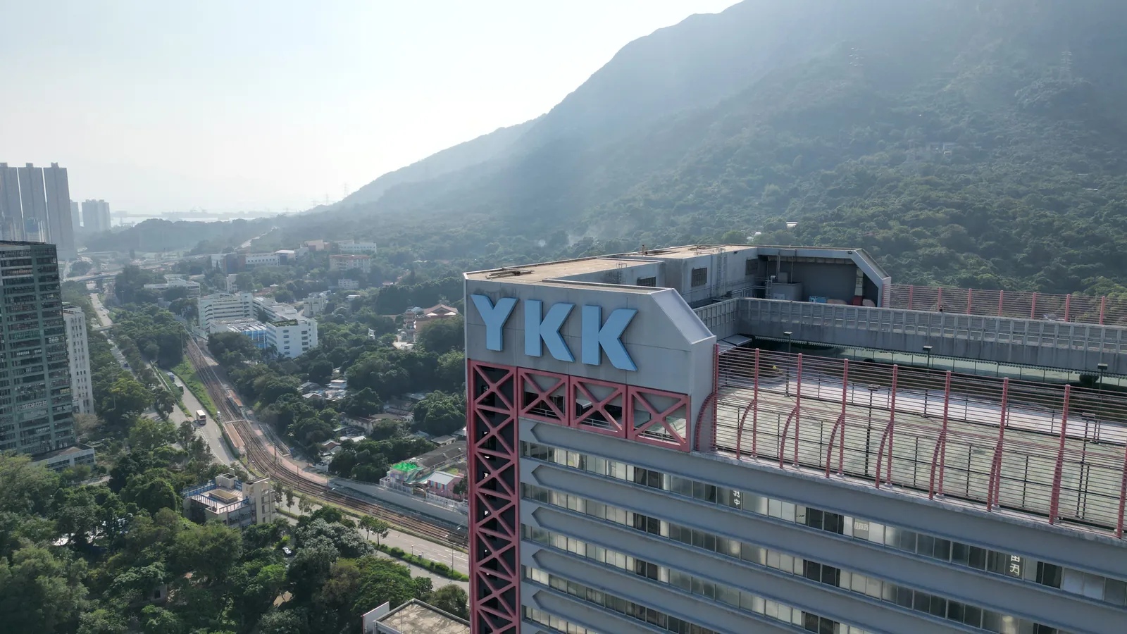 屯門吉田大廈高空外觀,屋頂 YKK 標誌後方可見山景及鐵路