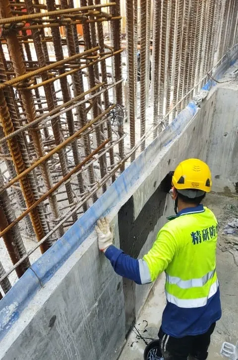 Worker applying dark material to a concrete wall base beneath reinforcement at the Wang Chau public housing site